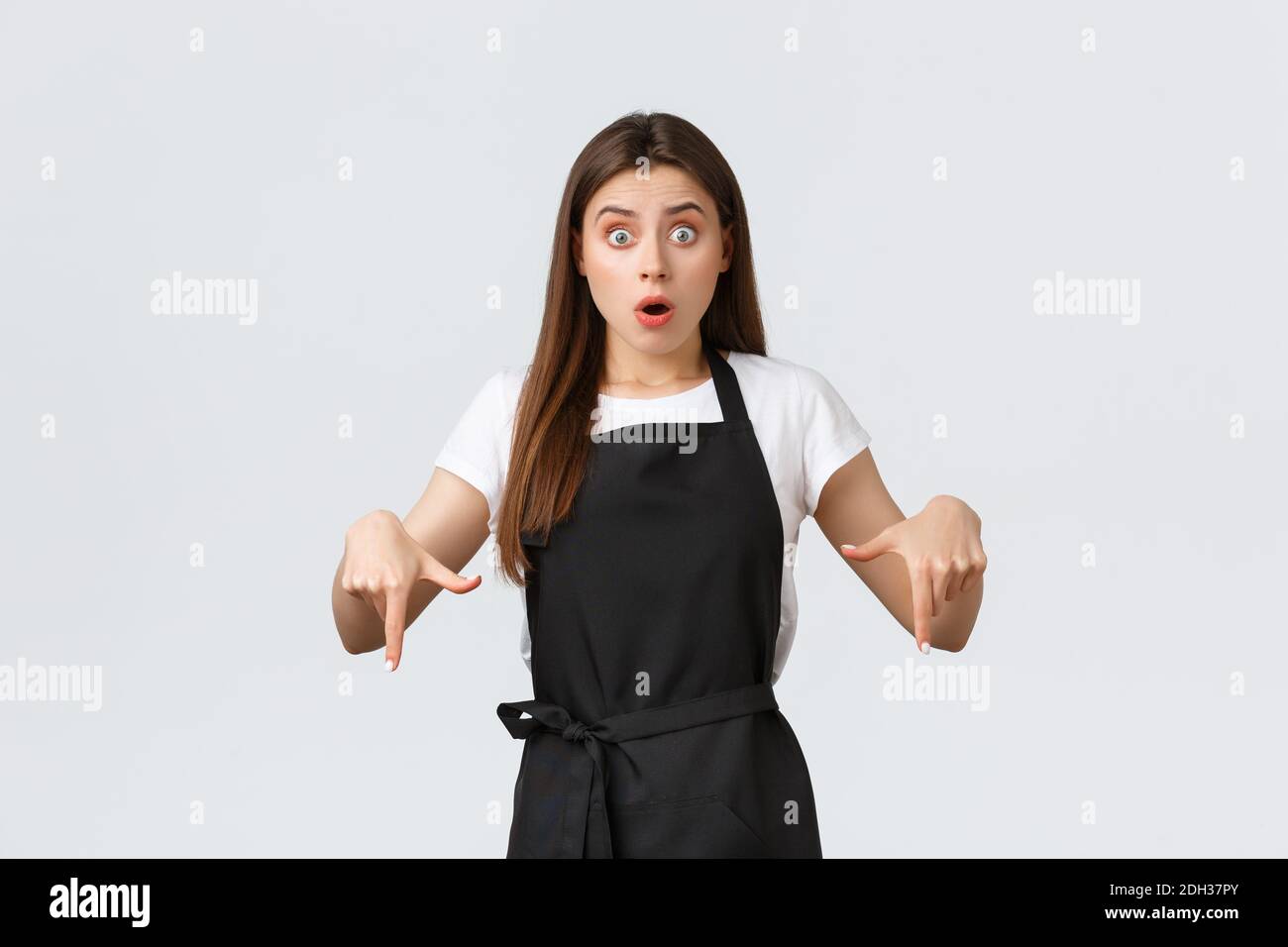 Piccola impresa, dipendenti e caffetteria. Cameriera preoccupata e scioccata che punta le dita verso il basso. Un barista confuso Foto Stock