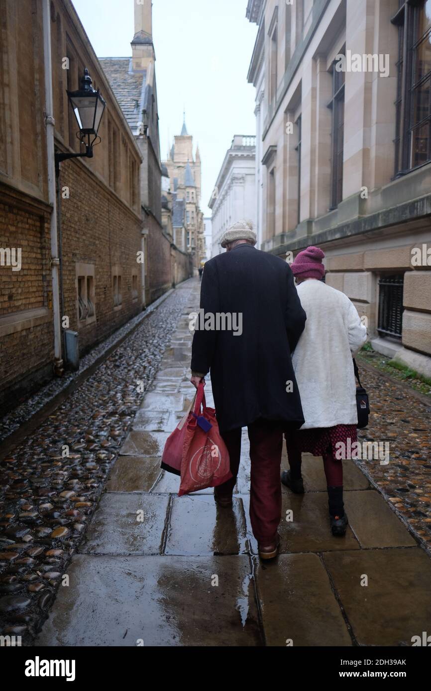 Cambridge UK Dicembre 2020 Vista posteriore di una coppia più anziana Camminando attraverso la strada del passaggio della Camera del Senato nel centro Della città di Cambridge con una pioggia fredda Foto Stock