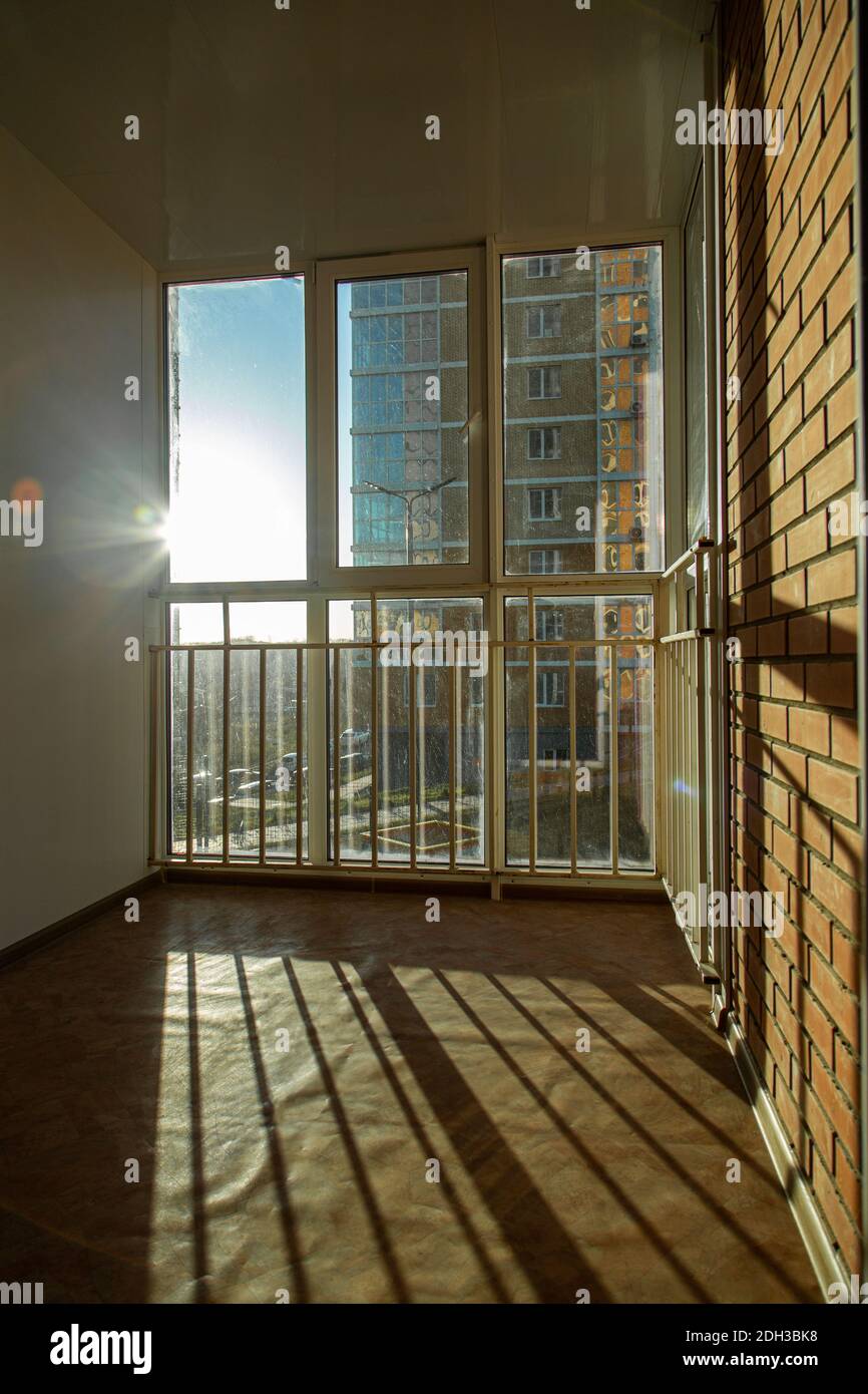 Il sole luminoso splende splendidamente attraverso la finestra sul balcone con barre e finestre in plastica. Gettare un'ombra su un muro di mattoni. Foto Stock