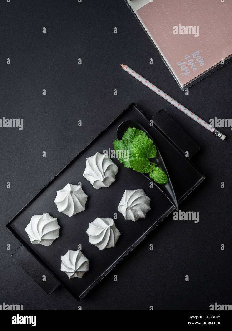 Meringa bianca dall'uovo bianco su vassoio nero Notepad e matita su sfondo nero. Scatto in testa. Foto Stock