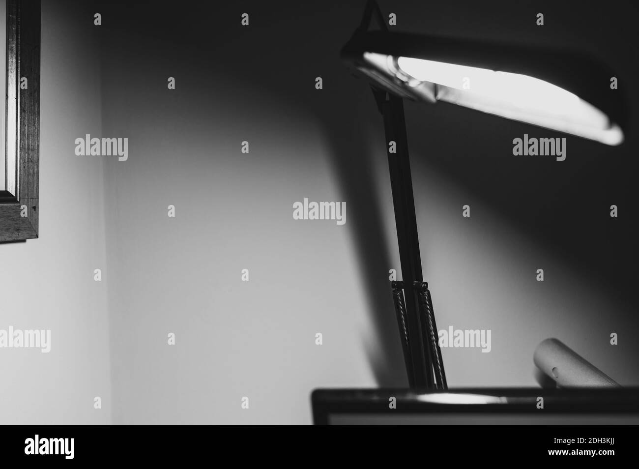 Immagine monocromatica in bianco e nero della lampada da tavolo articolata con le braccia nere in primo piano si sfocano e con la lampadina illuminata Con la sua ombra su wall.A Foto Stock