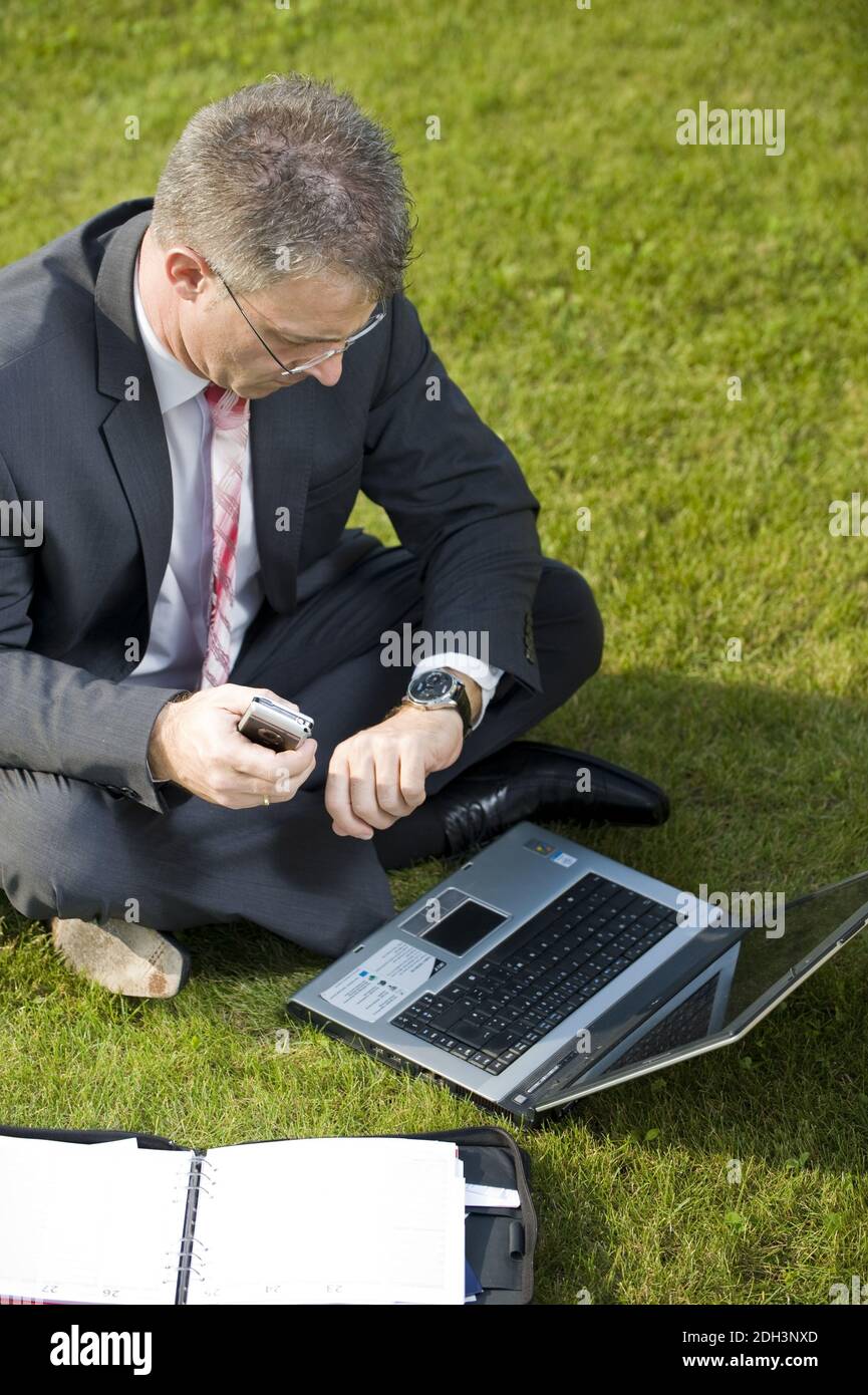 Geschäftsmann sitzt auf einer Wiese, schaut auf die Uhr, notebook, computer, signor:Sì Foto Stock