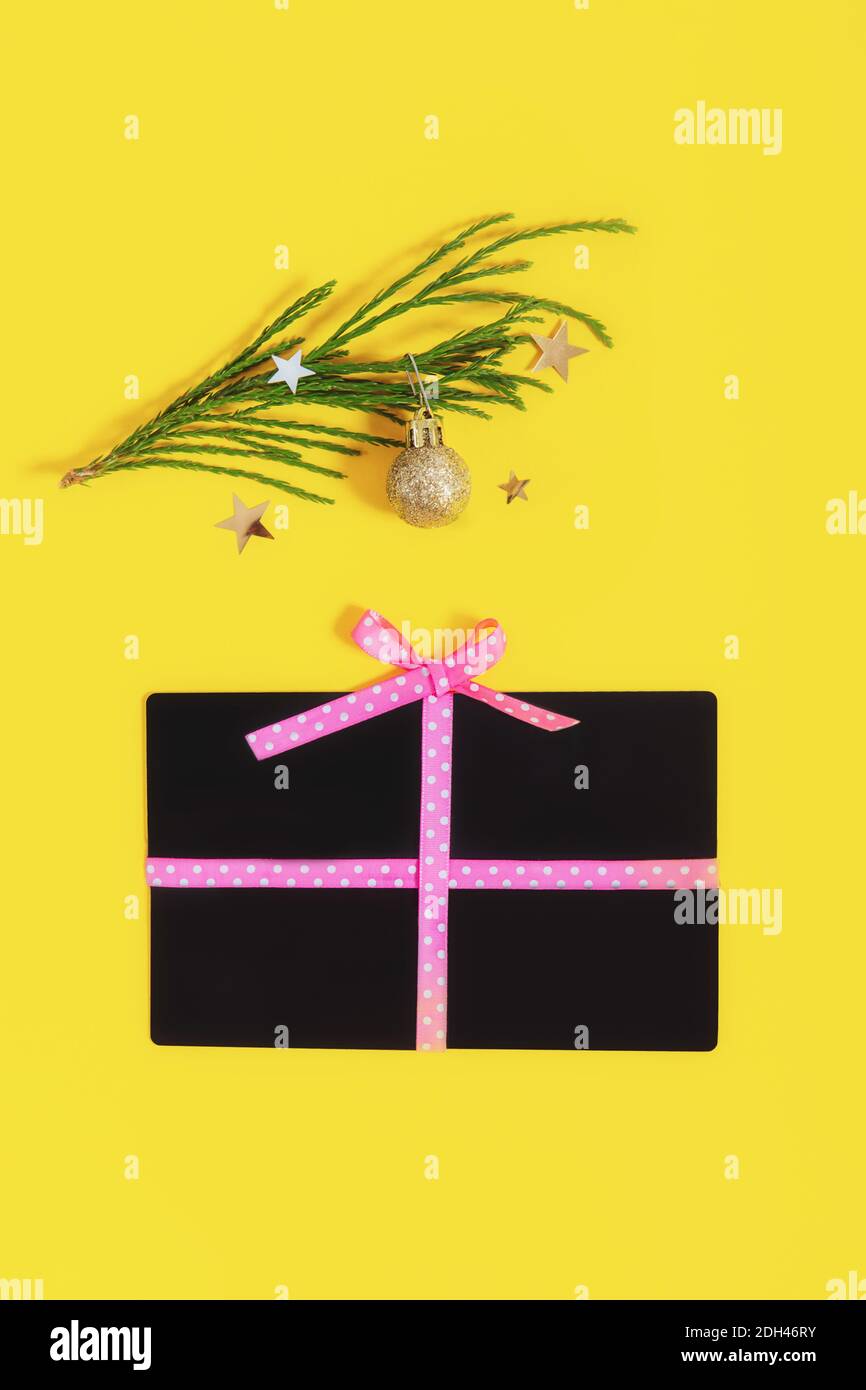 Forma piatta della scatola del regalo della disposizione con un arco fatto delle giftcards del negozio e delle sfere dorate ramo dell'albero di natale sul colore giallo di tendenza sfondo. Idee creative Foto Stock