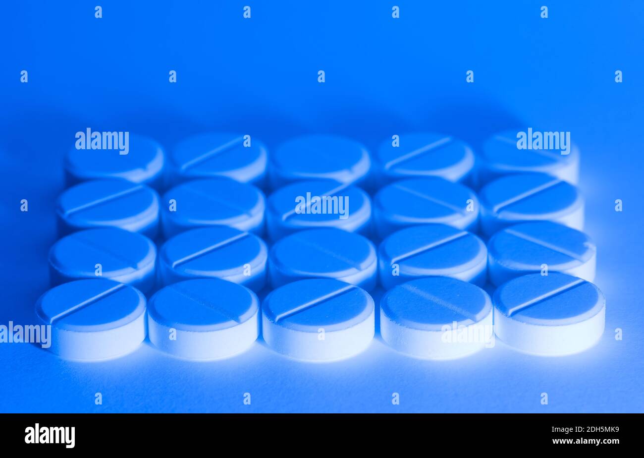 Pillole mediche bianche nella luce blu su sfondo bianco Foto Stock