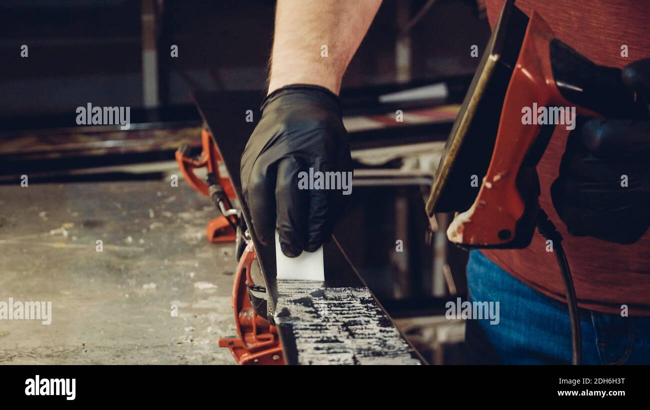 Applicazione di cera calda alla base da sci con il ferro da stiro. Applicazione della cera da sci alla base da sci. Sintonizzazione della base sci. Ferro da sci e barre di cera. Servizio sci AN Foto Stock