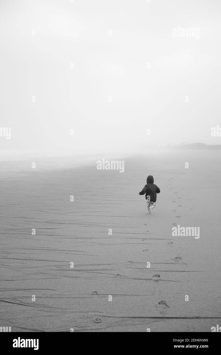 Ragazzo che corre sulla spiaggia a Coastal Fog Storm Foto Stock