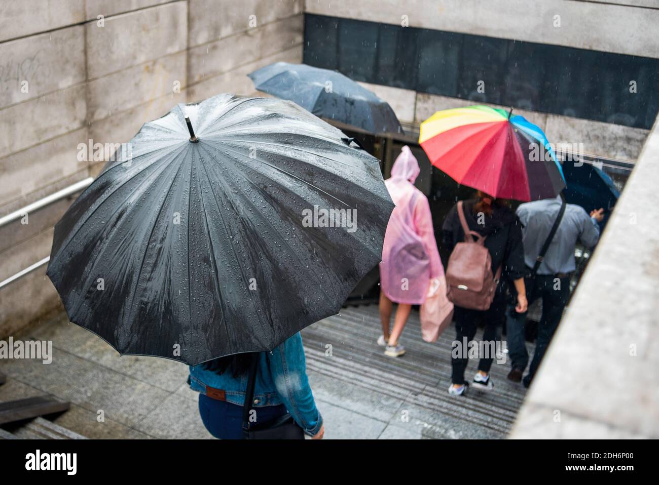 Le persone con ombrelloni scendono nel sottopassaggio. Paesaggio urbano in una giornata piovosa. Ombrello con gocce di pioggia. Maltempo. Stile cittadino. Foto Stock