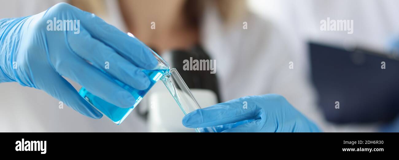 Mani di scienziato in guanti versando liquido blu nel test tubo Foto Stock