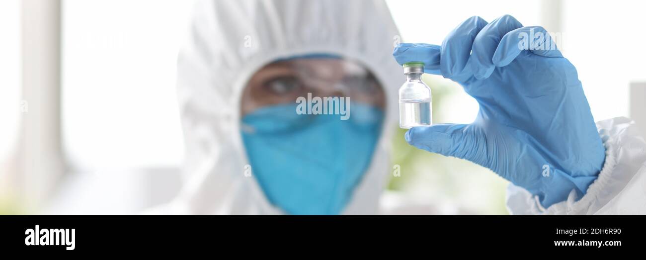 Ricercatore in tuta protettiva guarda flacone medicinale. Foto Stock