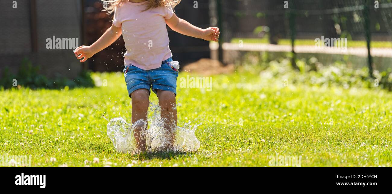 Bambino felice che corre attraverso l'acqua bagnata sprashinh del prato. Foto Stock