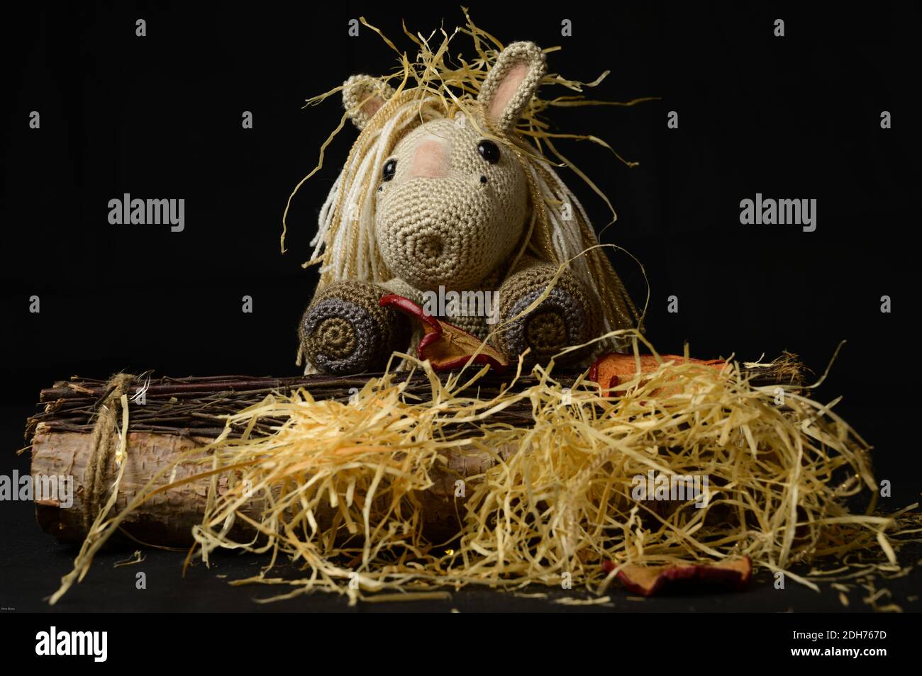 Un giocattolo a cavallo amigurumi uncinetto con paglia decorativa, pezzi di legno e ornamenti su sfondo nero Foto Stock