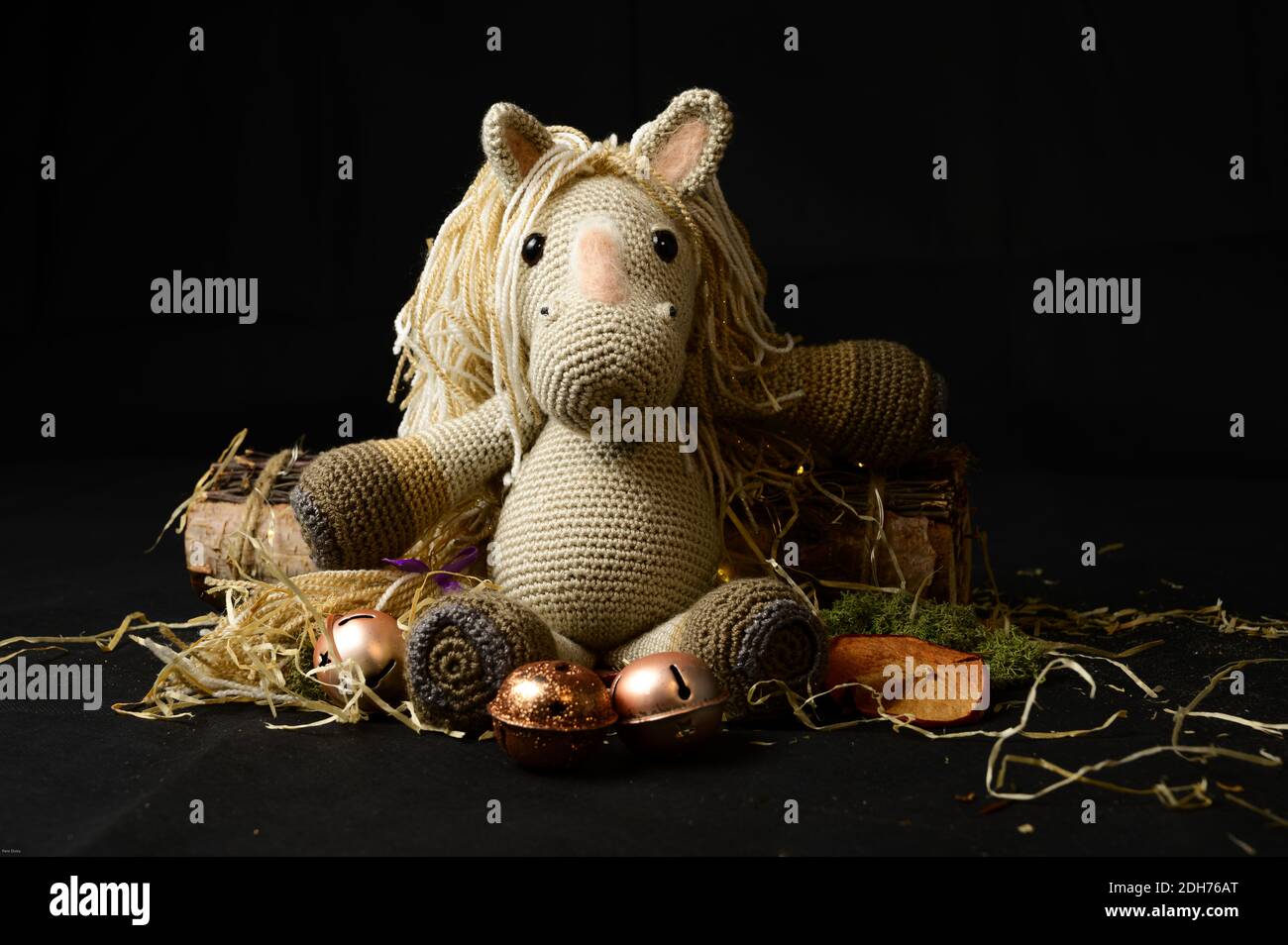 Un giocattolo a cavallo amigurumi uncinetto con paglia decorativa, pezzi di legno e ornamenti su sfondo nero Foto Stock