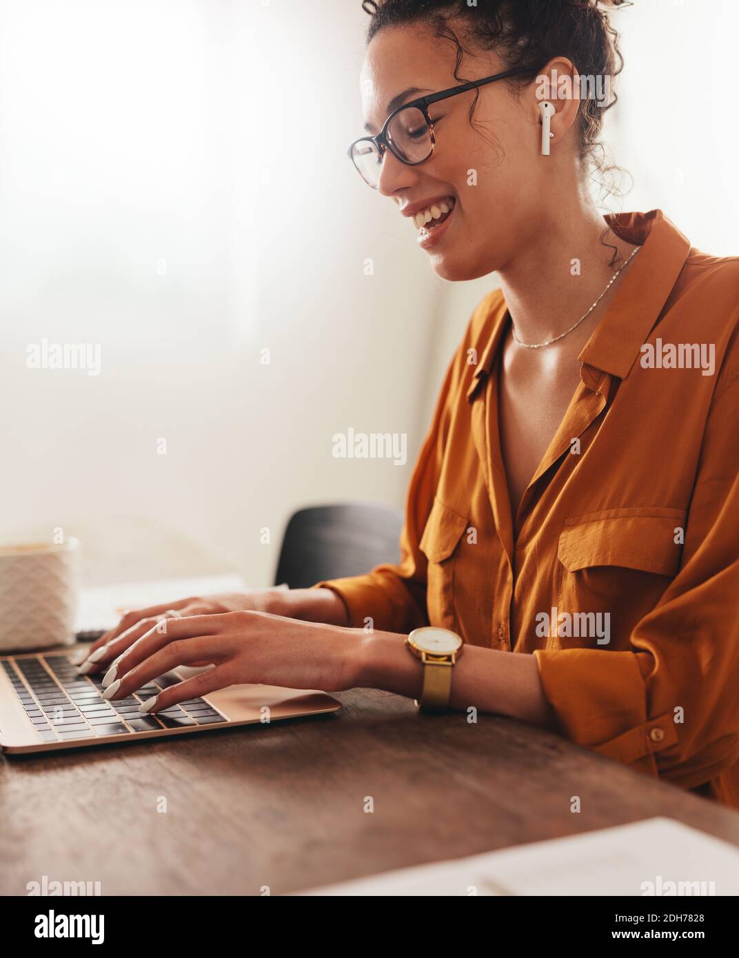 Donna sorridente mentre lavora con un notebook. donna d'affari che indossa auricolari wireless e utilizza un computer portatile a casa. Foto Stock