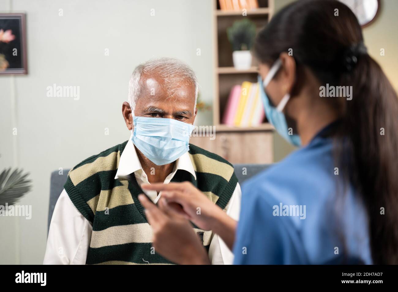 Spalla di Doctor che spiega come utilizzare l'app per la salute su mobile a uomo anziano durante la visita di casa mentre entrambi maschera facciale indossata - concetto di persone anziane Foto Stock