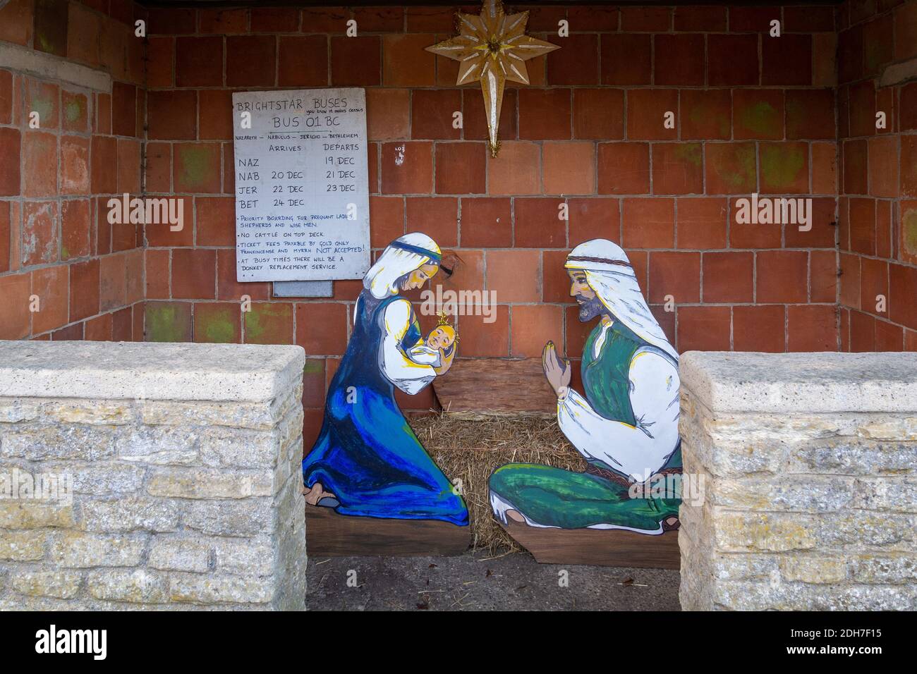 Presepio natalizio in un villaggio di rifugio autobus, Castle Ashby, Northamptonshire, Regno Unito; con un orario di autobus umoristico. Foto Stock