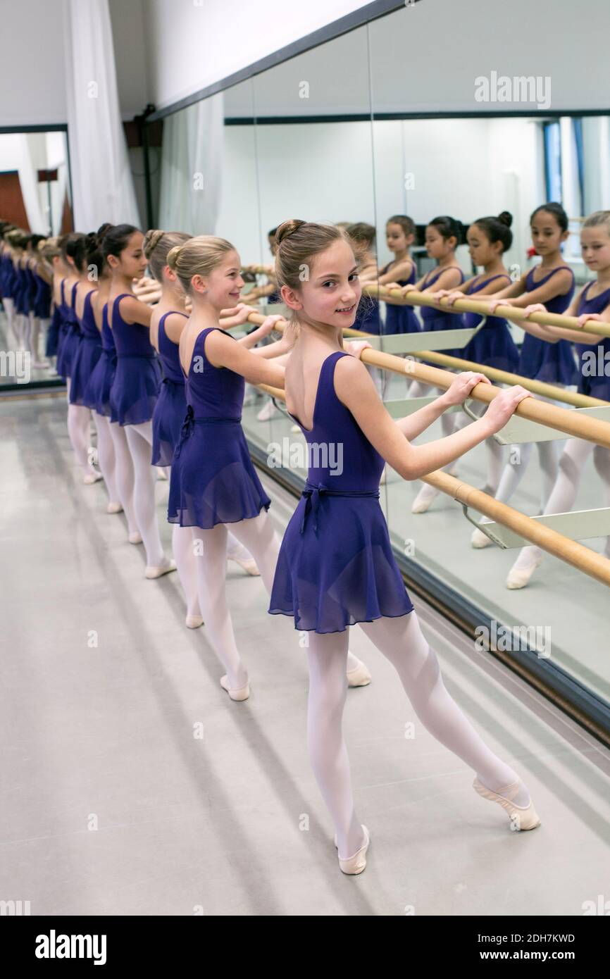 Piccole ballerine che usano barre mentre si pratica in studio di ballo.Ballerinas sono tutti vestiti per classe in leotards, tights e pantofole di balletto corrispondenti. Foto Stock