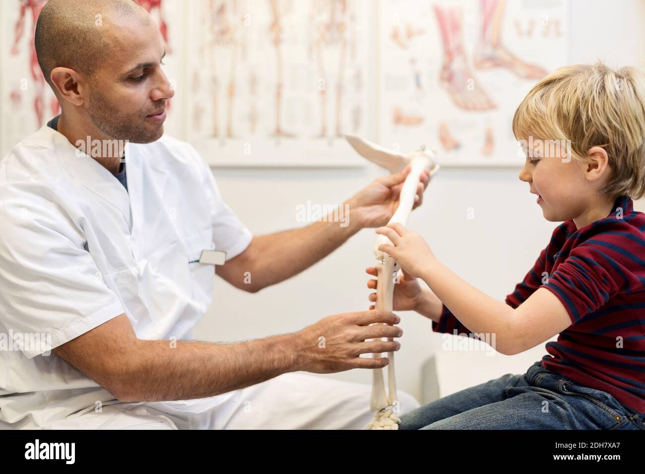 Ortopedista maschile che spiega modello di mano a ragazzo in clinica Foto Stock