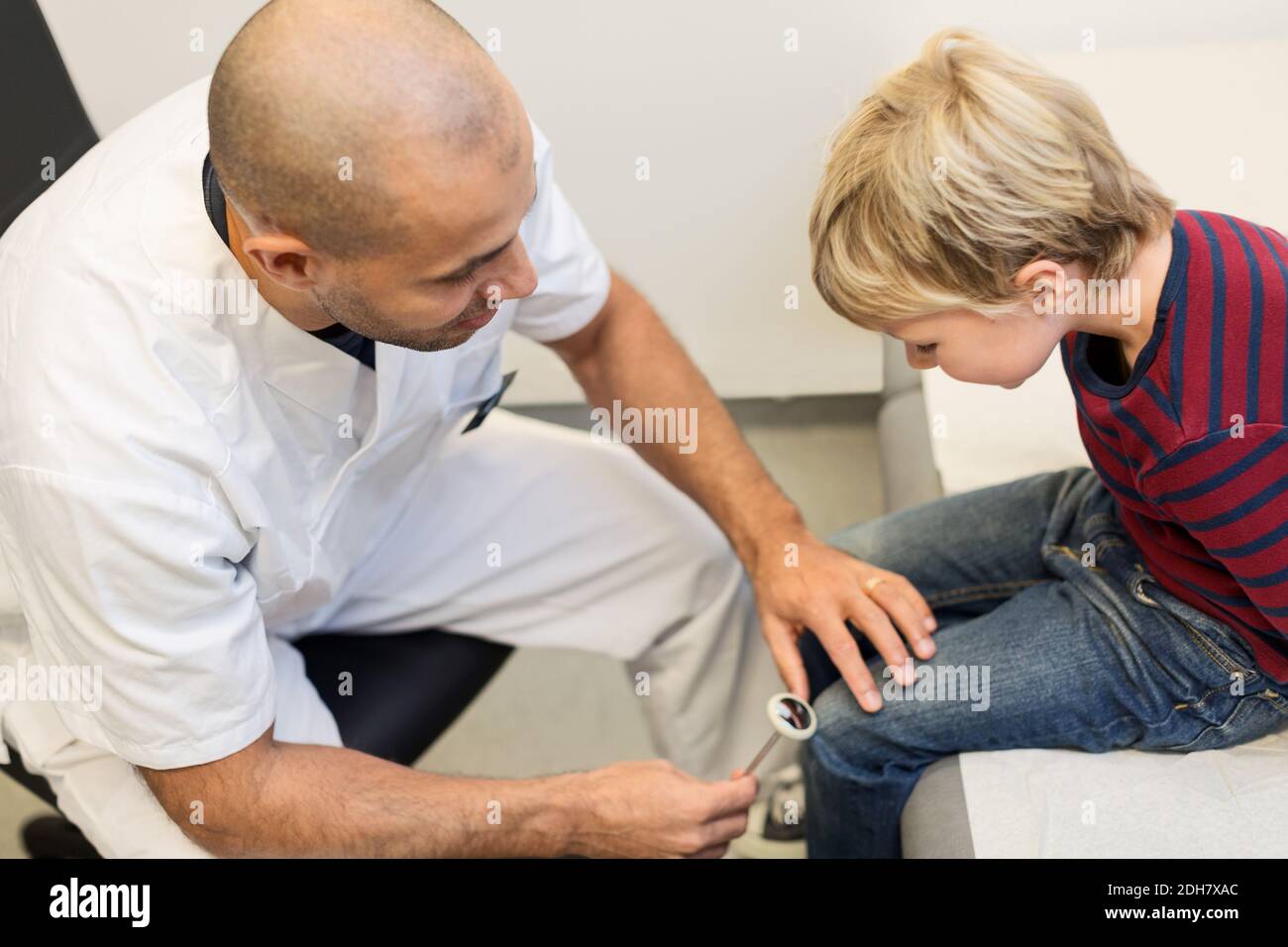 Ortopedico maschile controllo dei riflessi del ginocchio del ragazzo in clinica Foto Stock