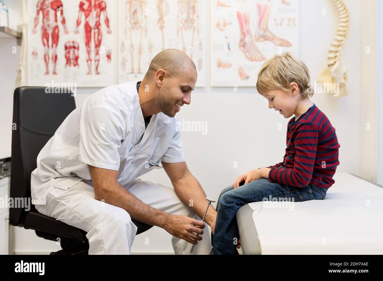 Medico di sesso maschile che controlla i riflessi del ginocchio del ragazzo in clinica ortopedica Foto Stock