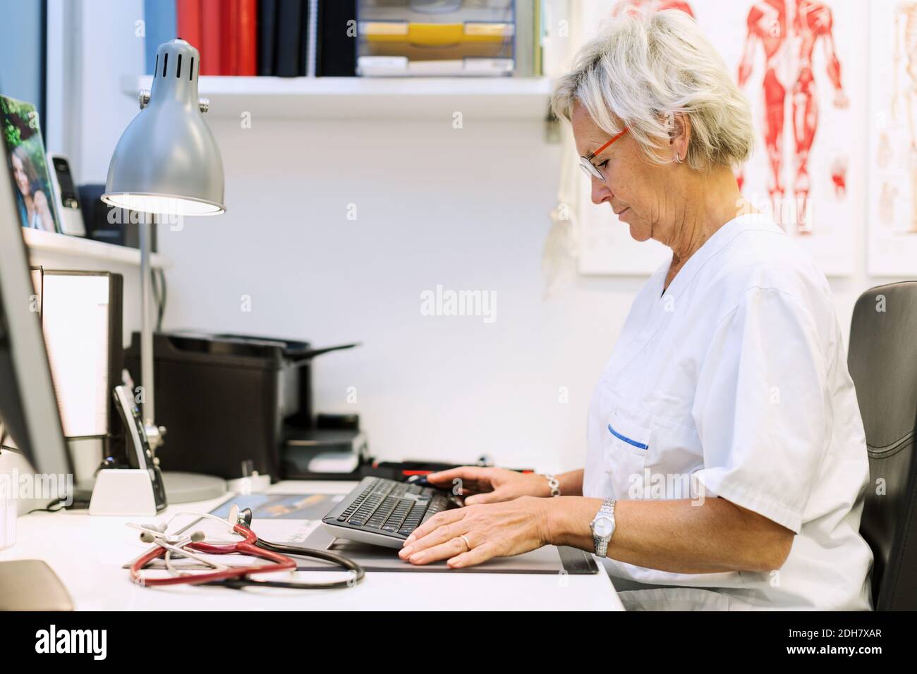 Vista laterale del chirurgo ortopedico senior utilizzando il computer alla scrivania in clinica Foto Stock