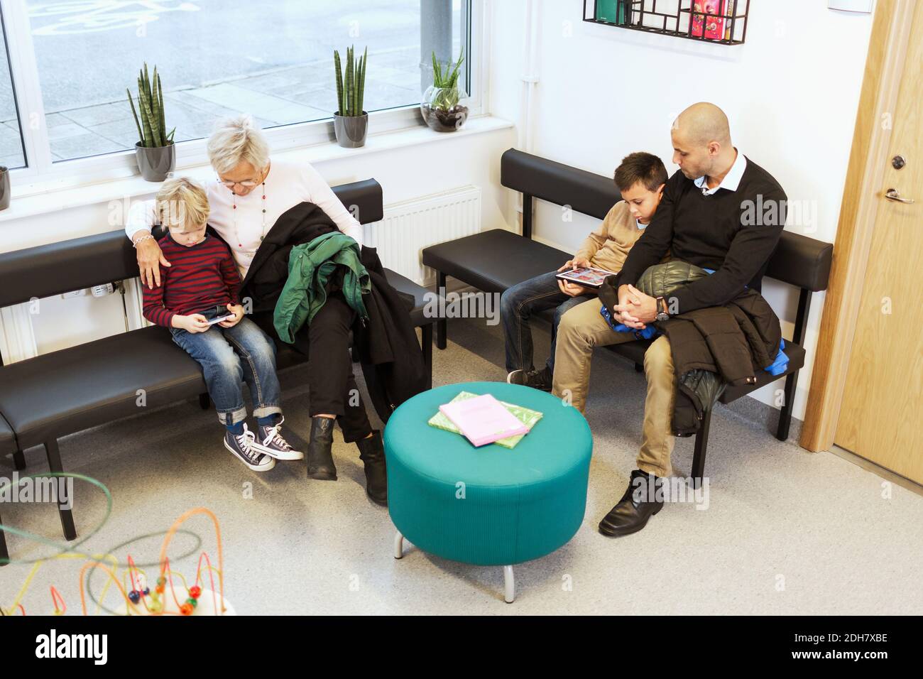 Famiglie che utilizzano tecnologie durante l'attesa in clinica ortopedica Foto Stock