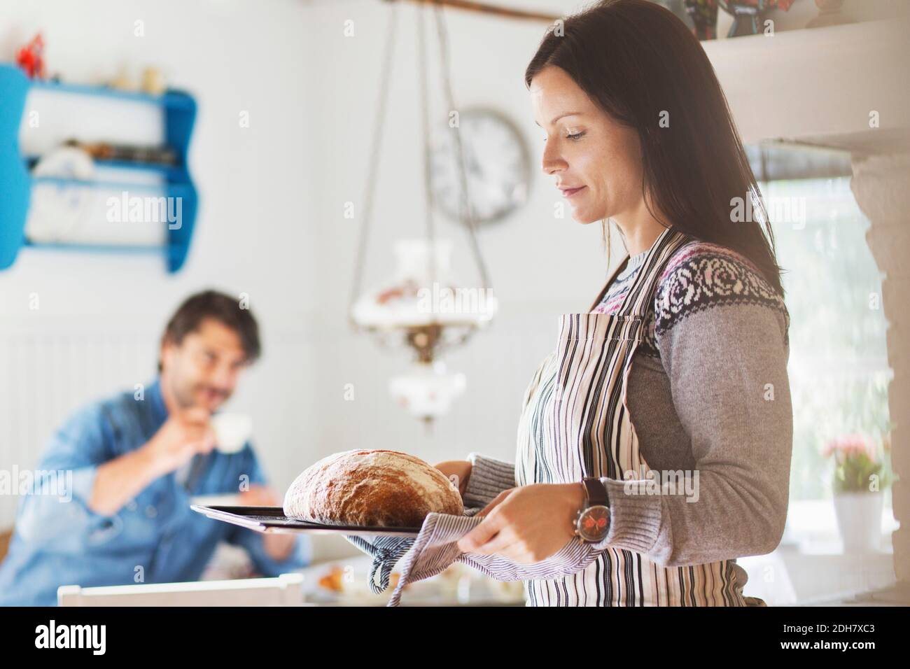 Donna che tiene il pane appena sfornato nel vassoio con l'uomo dentro sfondo a casa Foto Stock