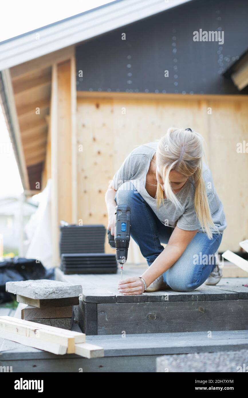 Tutta la lunghezza della donna che usa un cacciavite a batteria per il chiodo nel pavimento Foto Stock