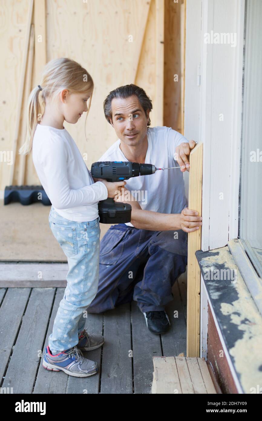 Padre che assiste la ragazza nell'uso del cacciavite senza fili mentre la casa migliora Foto Stock