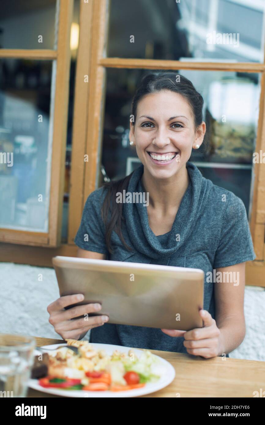 Ritratto di una donna felice che usa un tablet digitale mentre si pranza in caffetteria Foto Stock