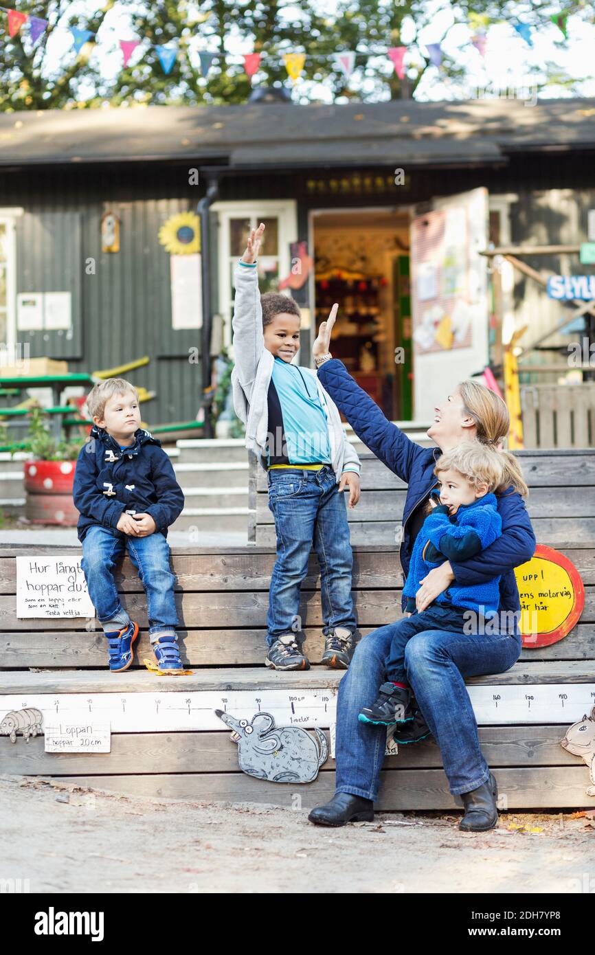 Felice insegnante che dà high-five fuori della costruzione di preschool Foto Stock