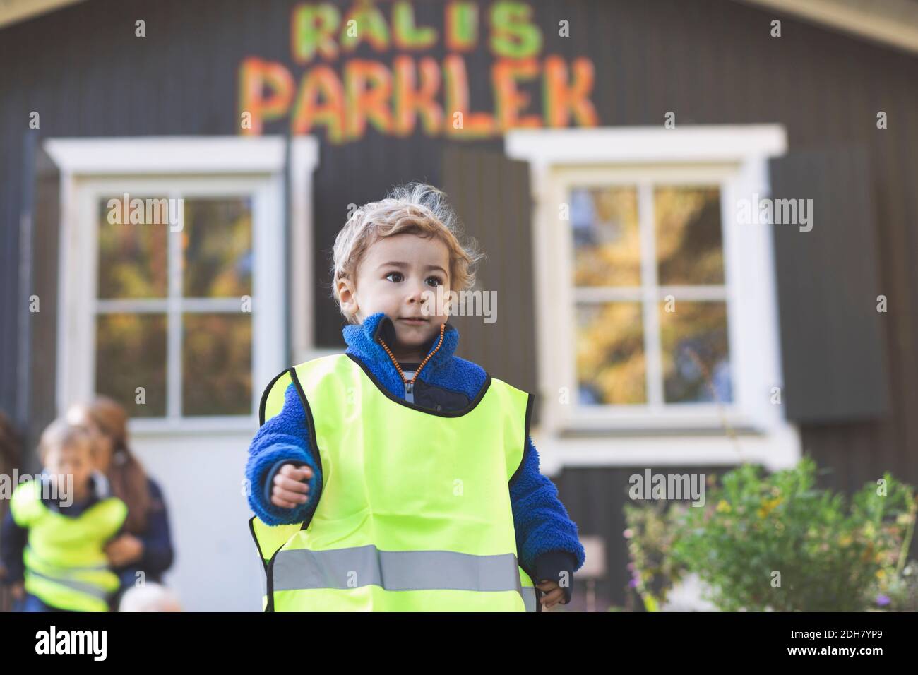 Ragazzo in giacca protettiva fuori dell'edificio prescolare Foto Stock
