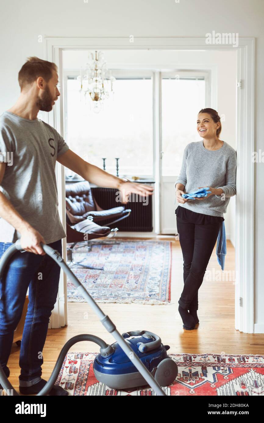 Uomo che usa l'aspirapolvere mentre parla con una donna a casa Foto Stock