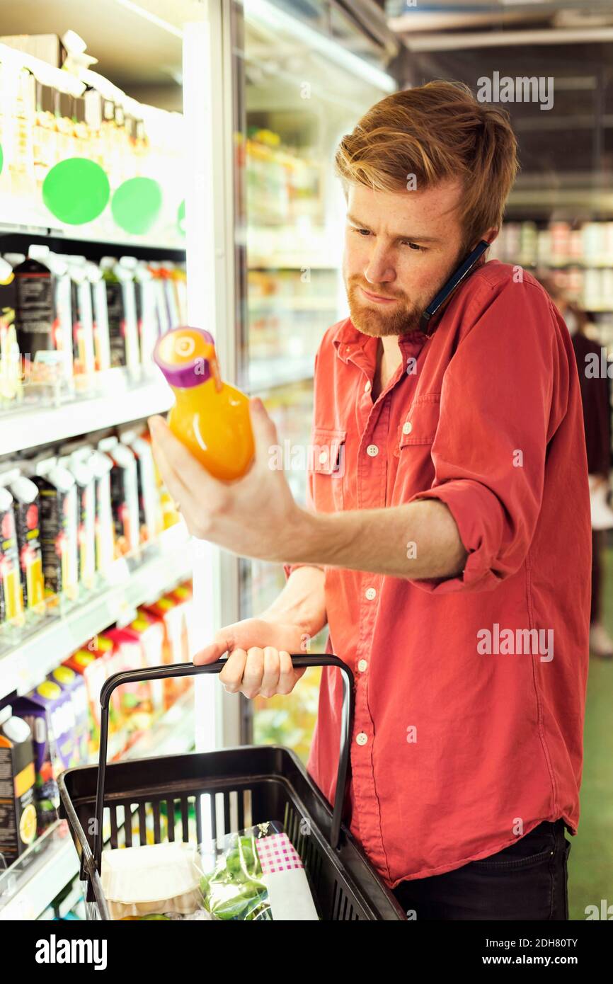 Uomo che risponde al telefono cellulare mentre si acquista la bottiglia di succo in freezer sezione nel supermercato Foto Stock