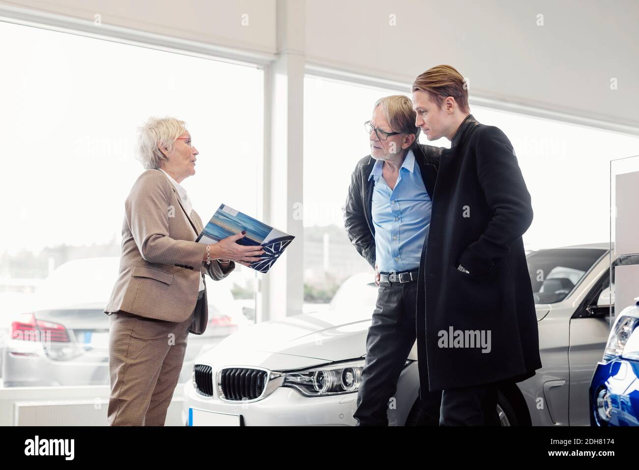 Venditore senior che spiega la brochure al figlio e al padre in auto negozio della concessionaria Foto Stock