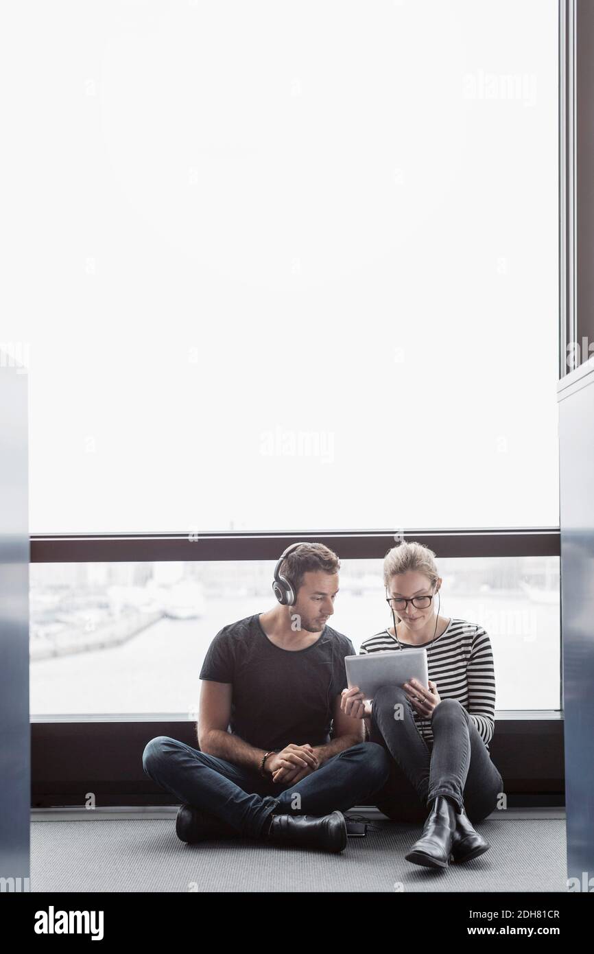 Colleghi aziendali che utilizzano il tablet digitale seduti accanto alla finestra ufficio Foto Stock