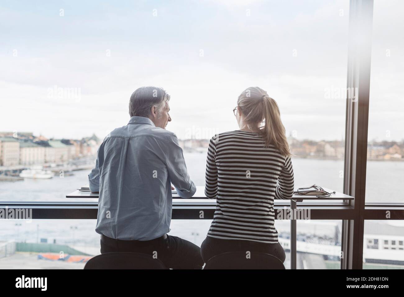 Vista posteriore degli uomini d'affari seduti al banco accanto alla finestra in ufficio Foto Stock