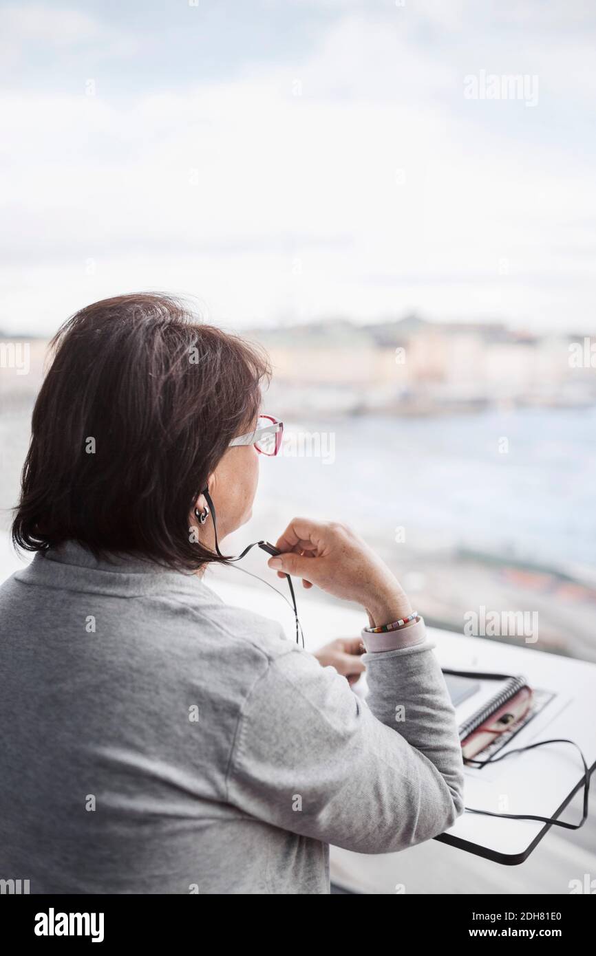 Vista posteriore della donna d'affari anziana che utilizza il dispositivo vivavoce tramite il finestrino in ufficio Foto Stock