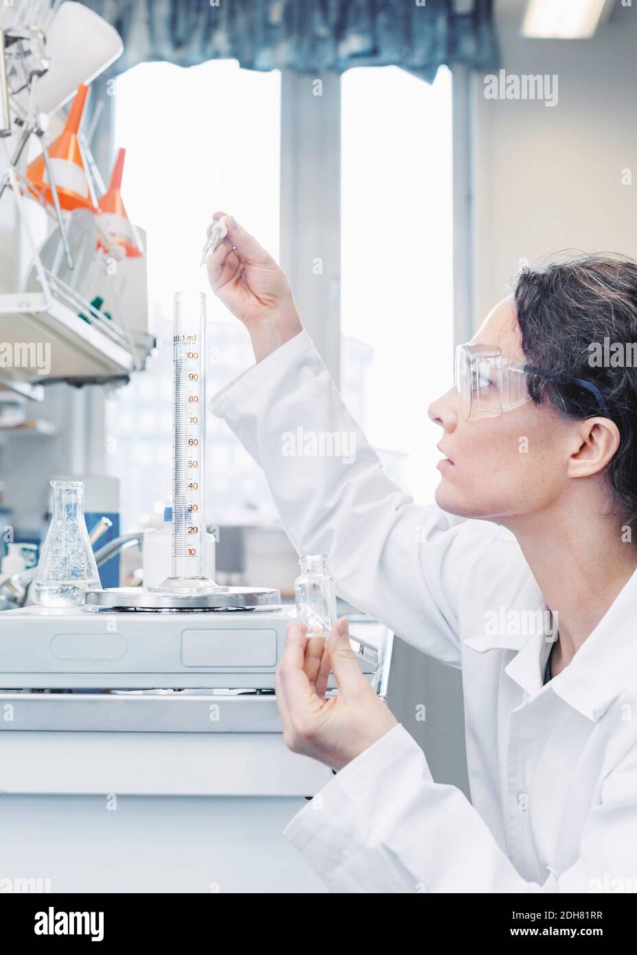 Scienziato femminile che versa il prodotto chimico in un becher in laboratorio Foto Stock