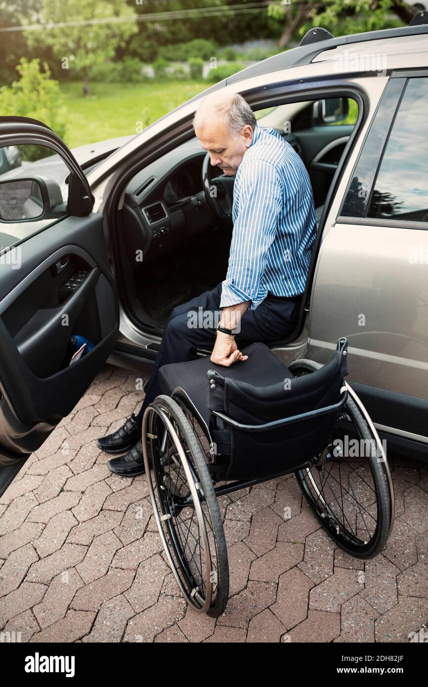 Uomo disabile che sbarchi dall'auto su sedia a rotelle Foto Stock