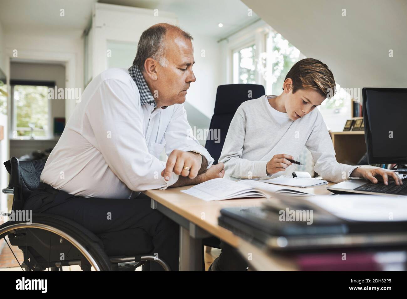 Il padre disabile assiste il figlio nel fare i compiti a casa Foto Stock