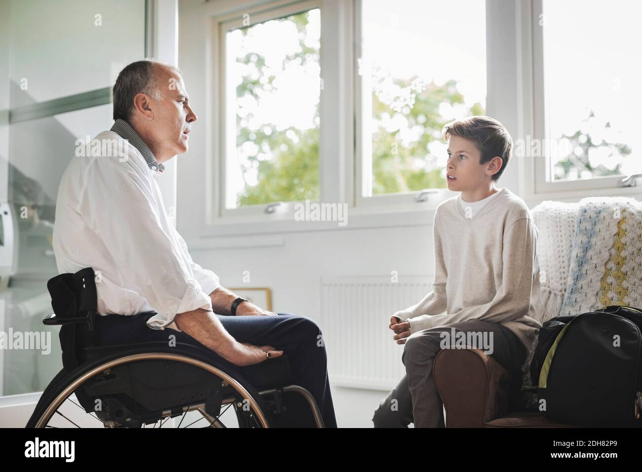 Padre disabile in sedia a rotelle che parla con il figlio a casa Foto Stock