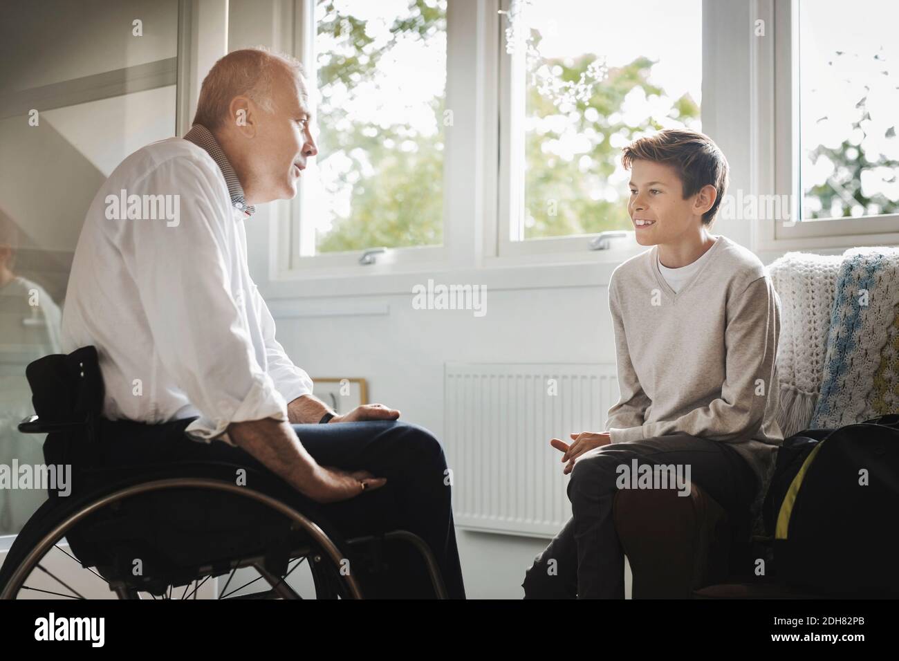 Uomo disabile in sedia a rotelle che parla con il figlio a casa Foto Stock