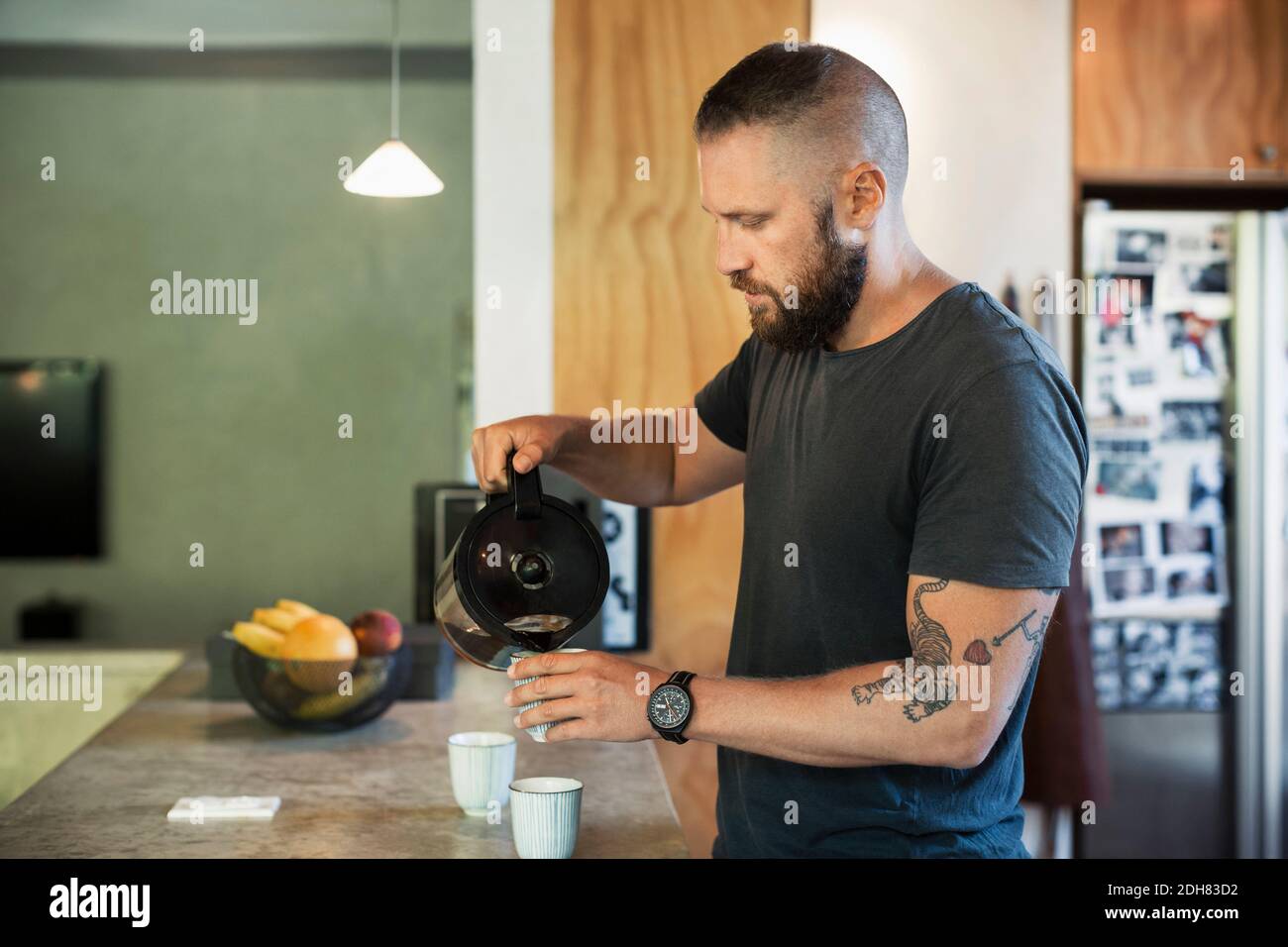 Uomo che versa il caffè in una tazza in cucina a casa Foto Stock