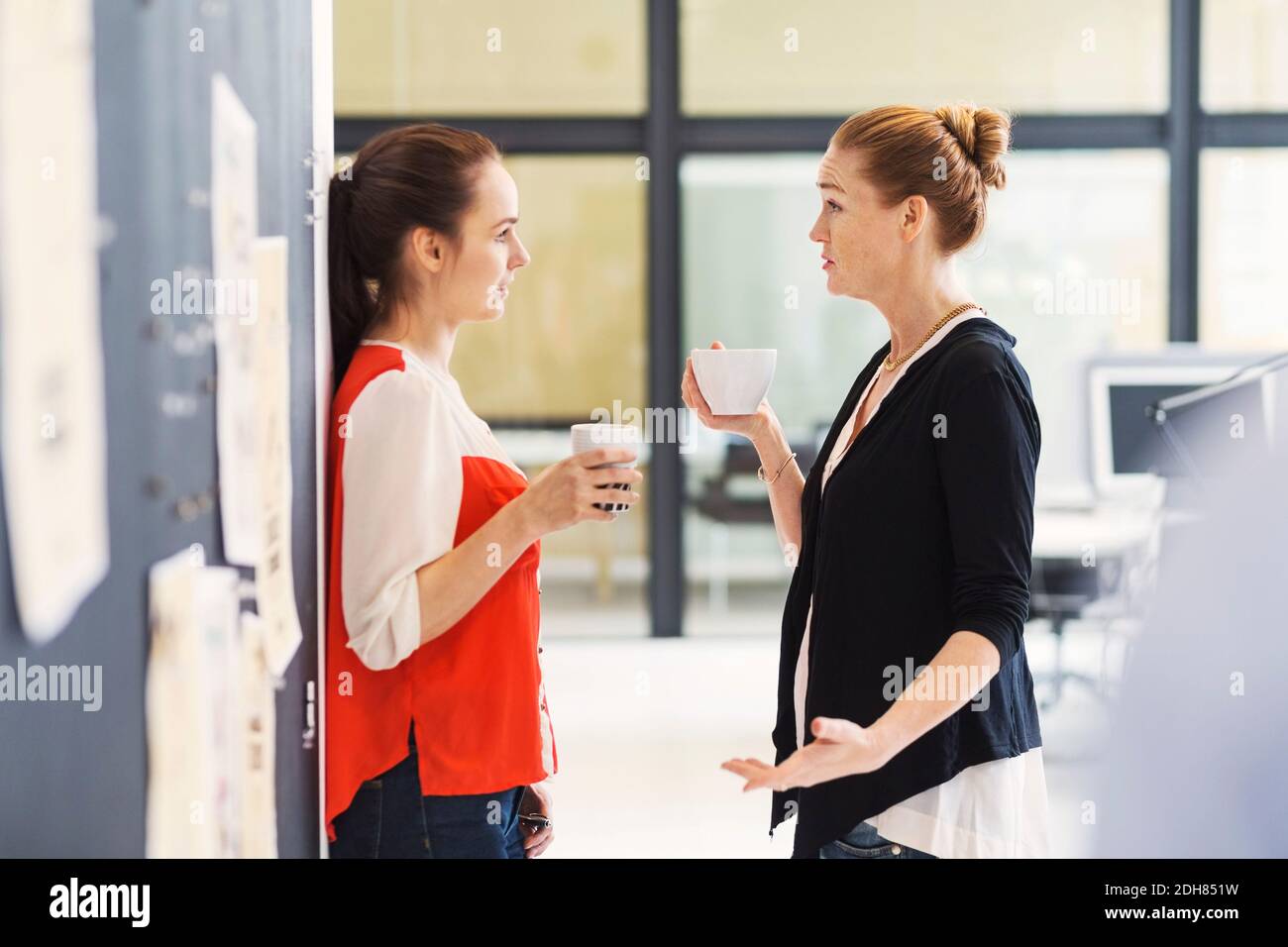 Vista laterale delle donne d'affari che discutono mentre hanno il caffè in ufficio Foto Stock