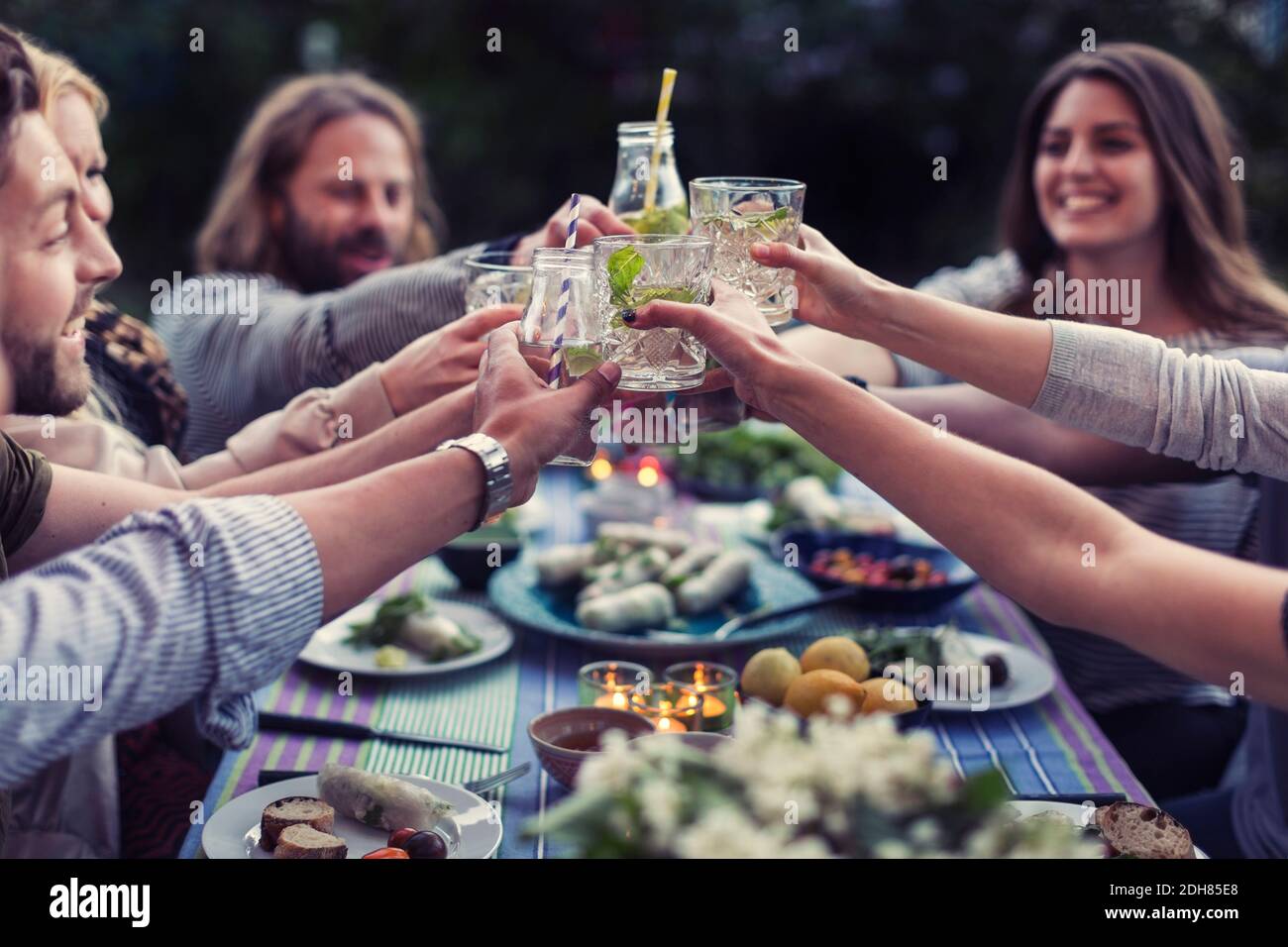 Amici felici che tostano i bicchieri di mojito al tavolo da pranzo in cortile Foto Stock
