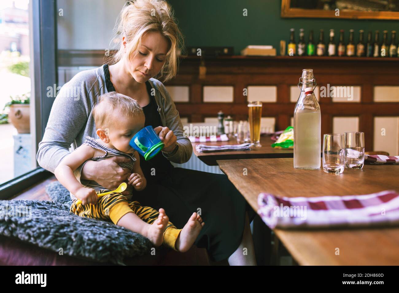 Donna mid adulta che alimenta l'acqua al figlio nel ristorante Foto Stock