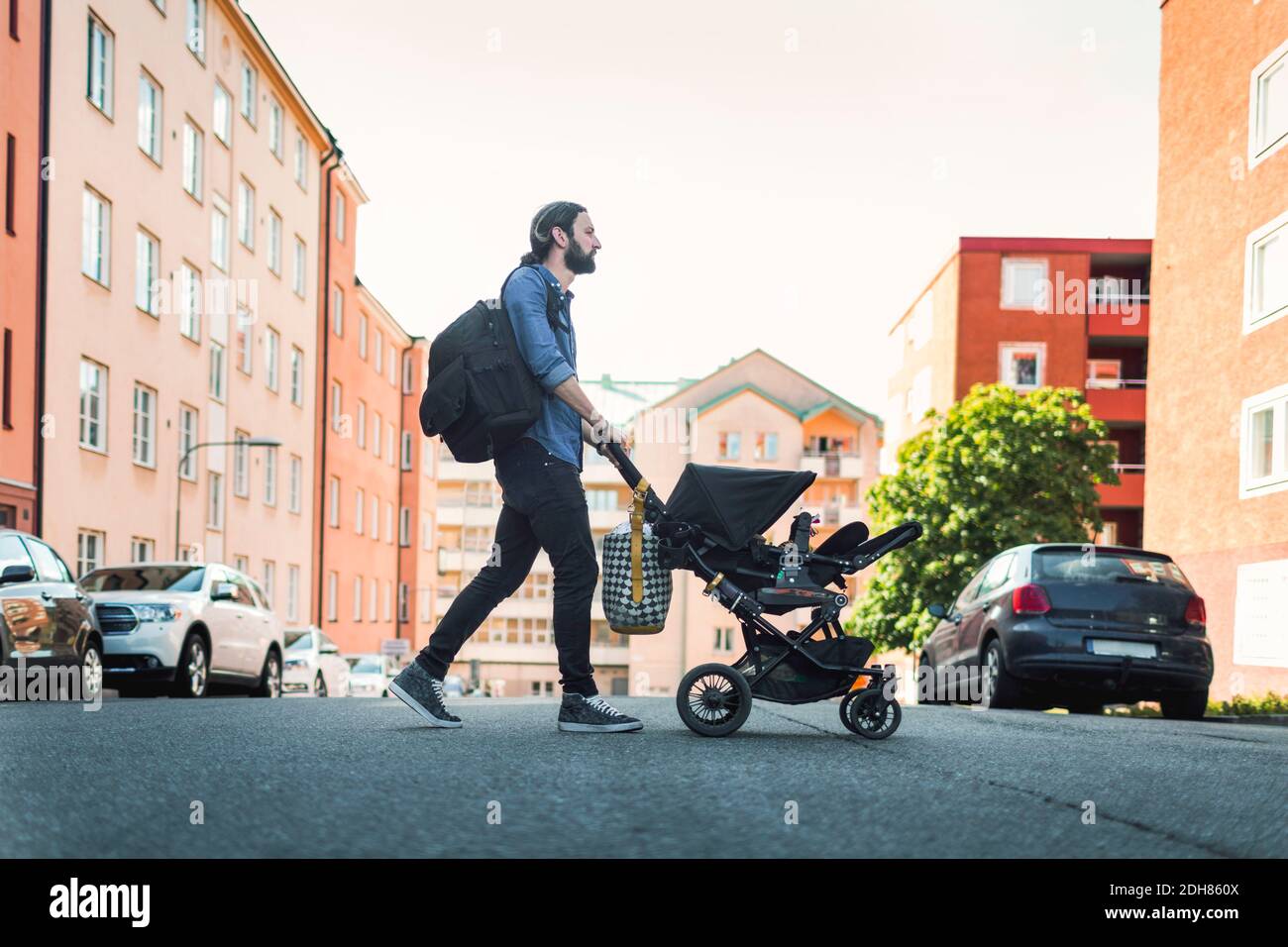 Vista laterale completa dell'uomo che spinge il bambino nel carrello attraversando la strada della città Foto Stock