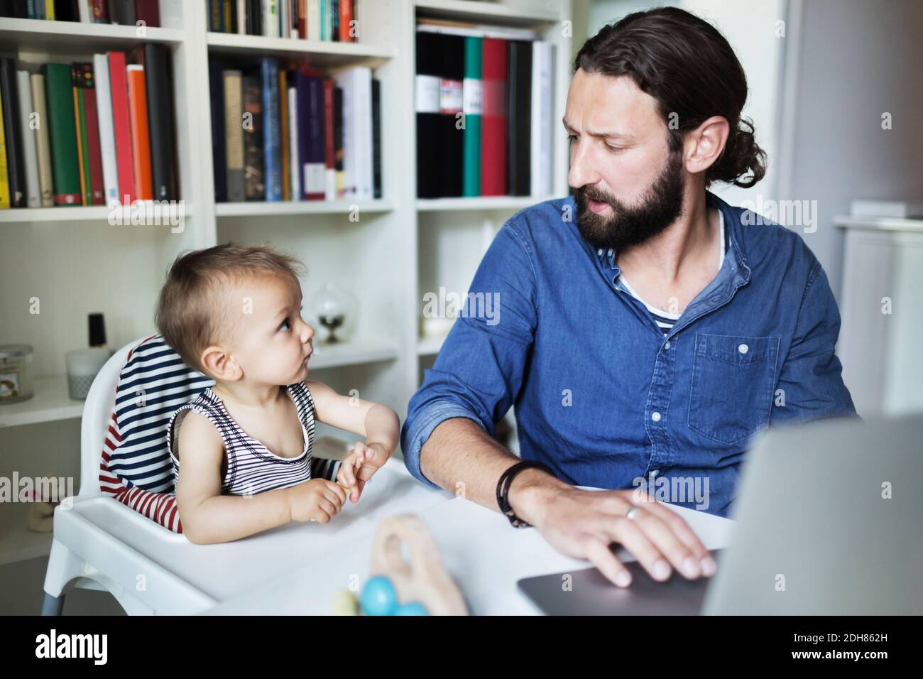 Uomo d'affari medio adulto che usa il laptop mentre guarda il bambino ragazzo a casa Foto Stock