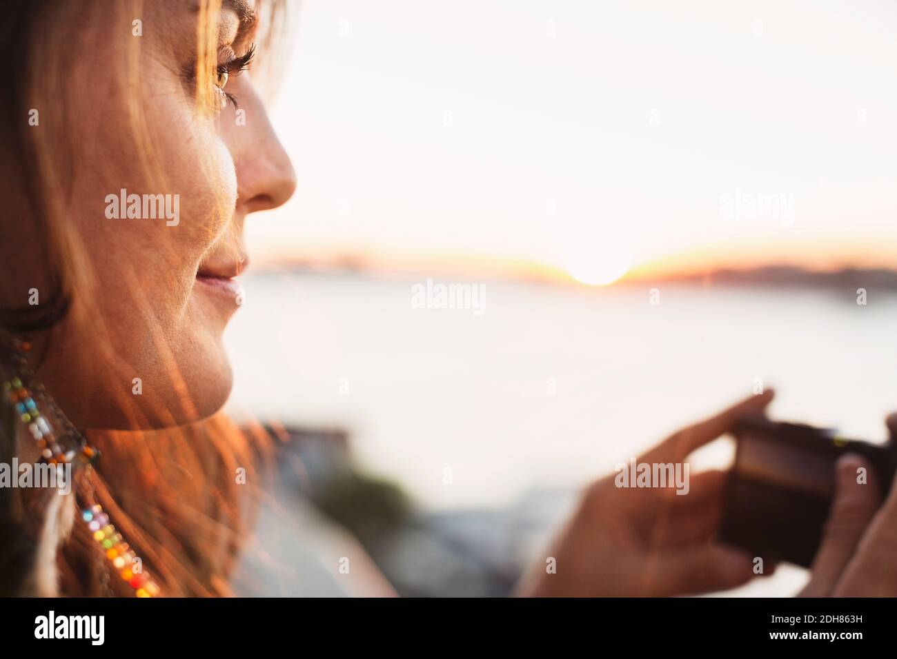 Immagine ritagliata del turista femminile che guarda via mentre tiene il digitale fotocamera contro il cielo limpido Foto Stock