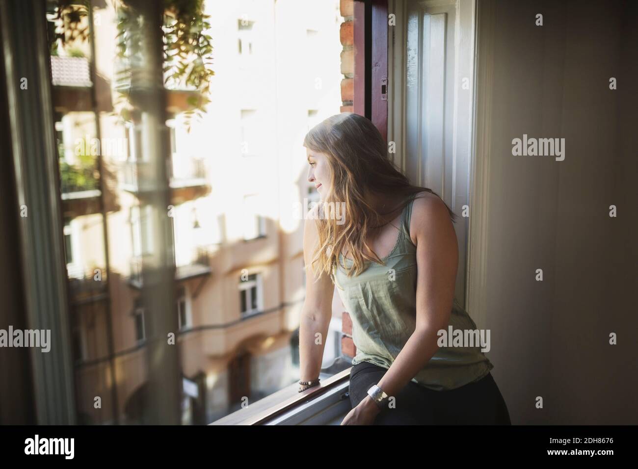 Giovane donna guardando attraverso la finestrella a casa Foto Stock